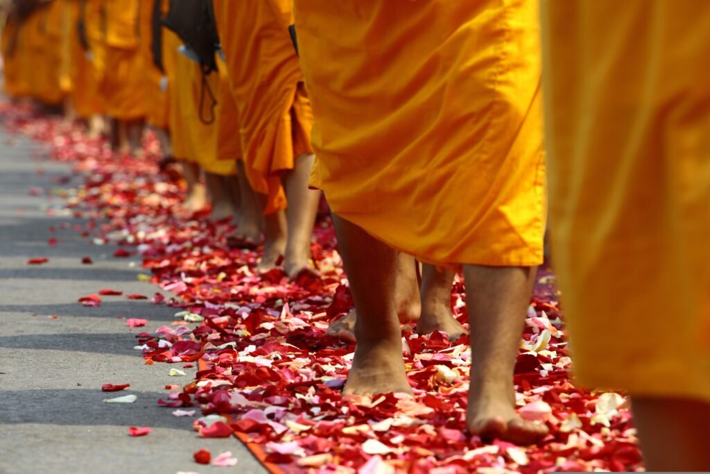 Barefoot monks in orange robes walk over scattered flower petals, reflecting the rituals and encounters of travel culture.