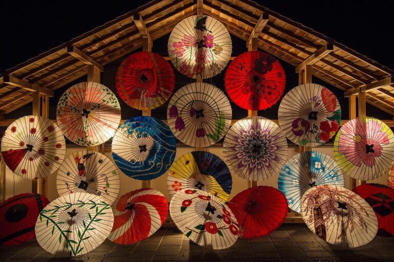 Colorful Japanese umbrellas arranged in a decorative display, featuring various patterns and designs against a dark background.