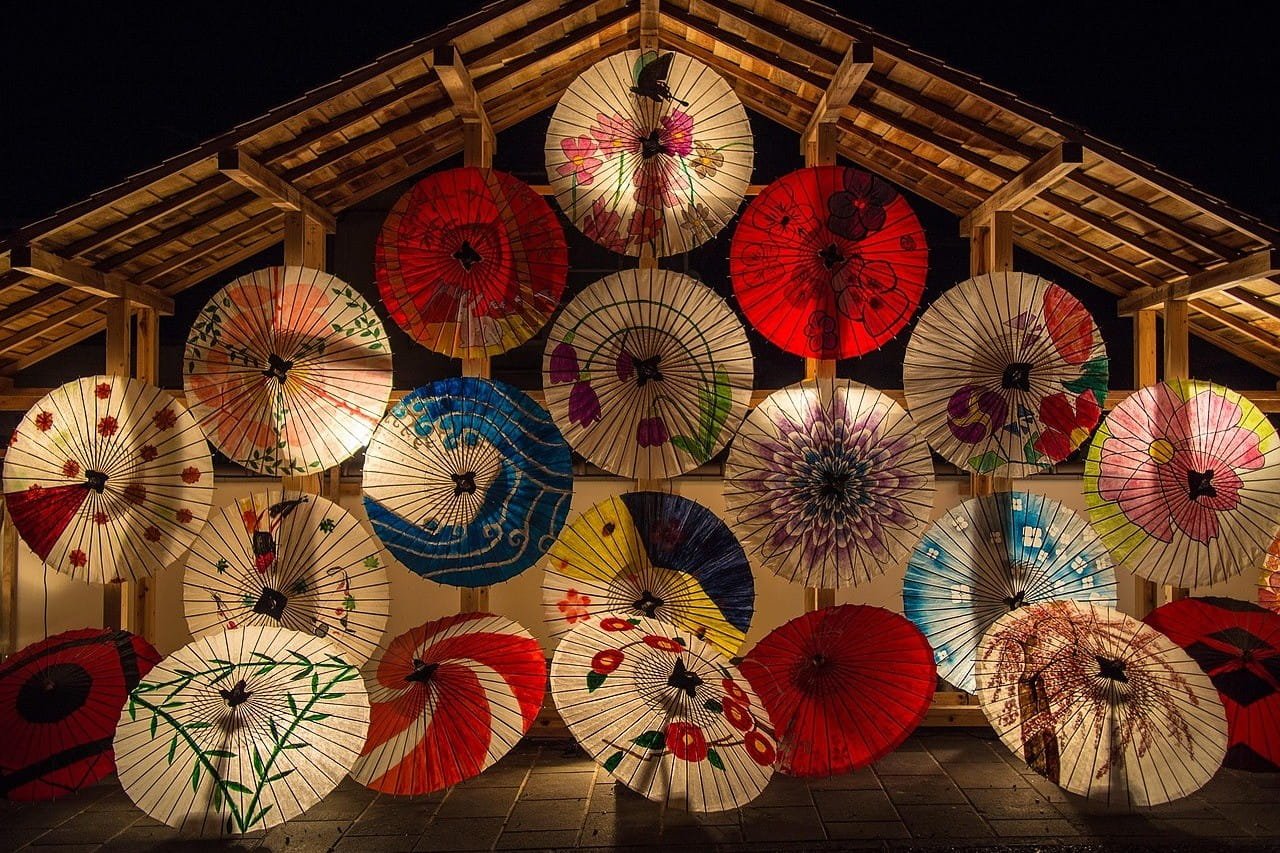 Colorful Japanese umbrellas arranged in a decorative display, featuring various patterns and designs against a dark background.