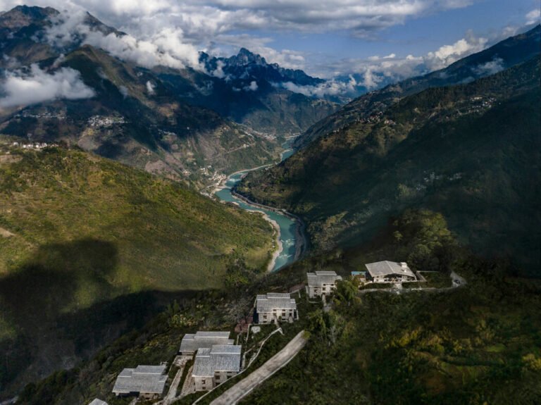 Aerial view of mountainous terrain with a winding river and scattered buildings nestled in the landscape.